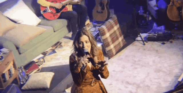 a woman singing into a microphone while a man plays a guitar in the background