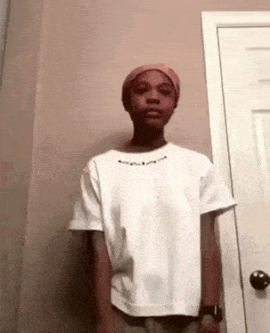 a young man wearing a white t-shirt and a hat is standing in front of a door .