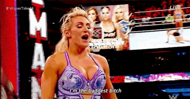 a woman in a purple dress is standing in a wrestling ring and says `` i 'm the baddest bitch ''