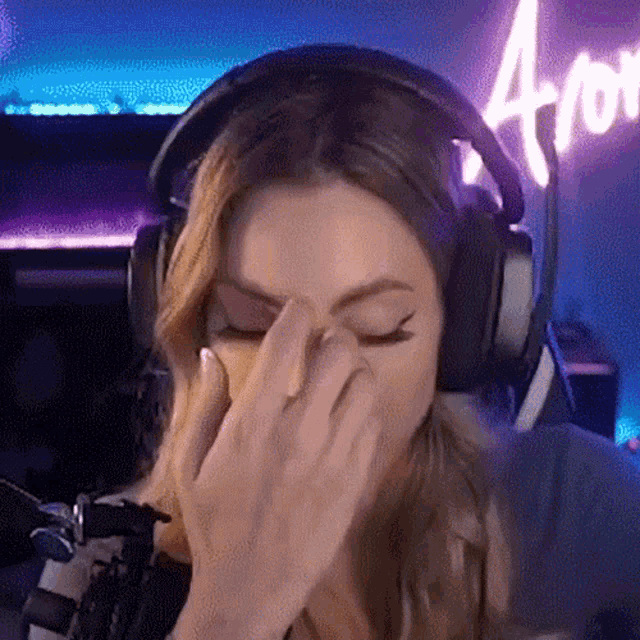 a woman wearing headphones is covering her face in front of a neon sign that says aro