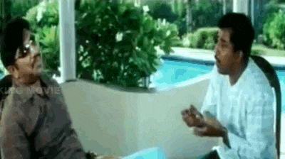 two men are sitting on a couch talking to each other in front of a swimming pool .