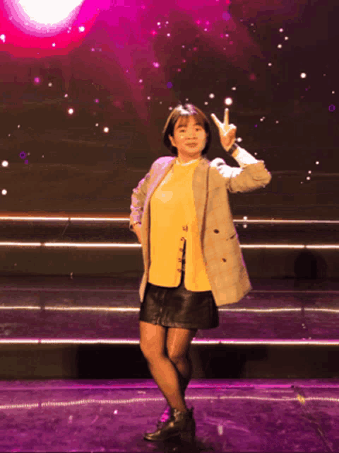 a woman in a yellow shirt and a plaid jacket is giving a peace sign