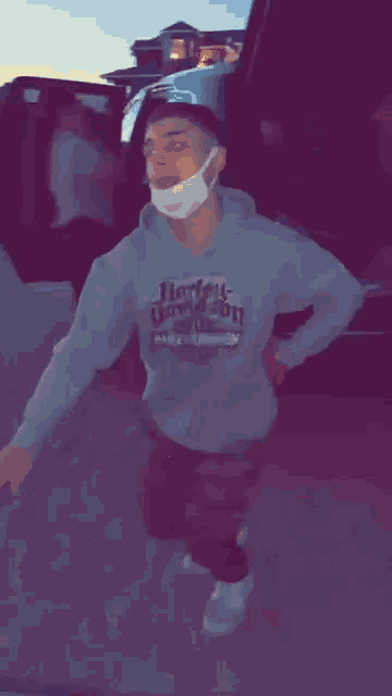 a man wearing a harley davidson hoodie and a mask is standing in front of a car .
