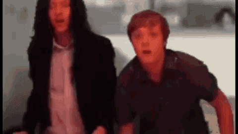 two men are standing next to each other in a room and looking at something .