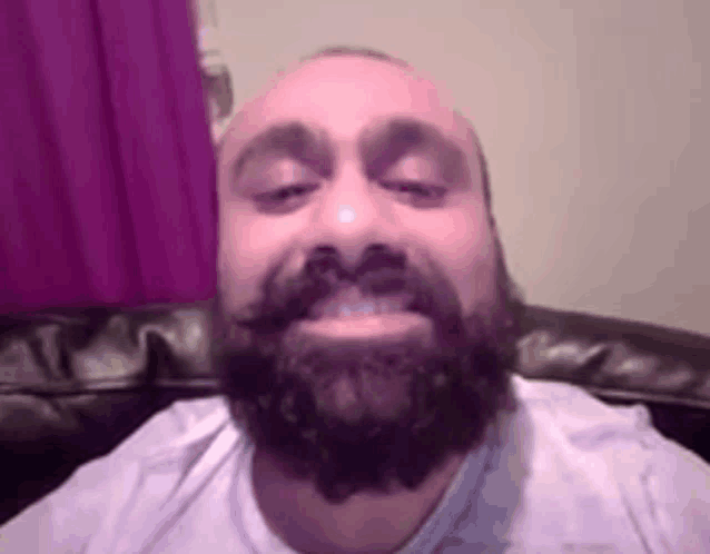 a man with a beard and mustache is sitting on a couch looking at the camera .