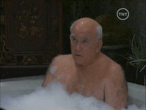 a bald man is taking a bath in a bathtub with a tnt logo on the bottom