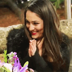 a woman is smiling while sitting at a table with flowers in front of her .