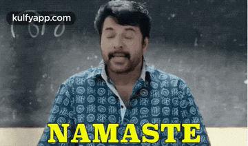 a man in a blue shirt is saying namaste in front of a blackboard .