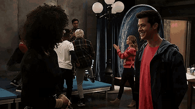 a man in a red shirt is standing in front of a group of people and says yeah i got you