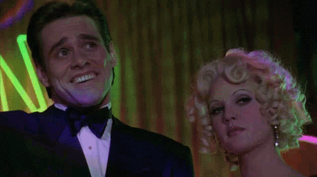 a man in a tuxedo stands next to a woman in a wig