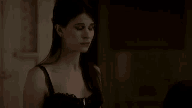 a woman in a black bra is standing in a dark room looking at the camera .