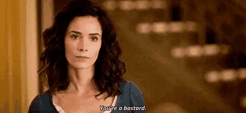 a woman with curly hair is standing in front of a mirror and says `` you 're a bastard '' .