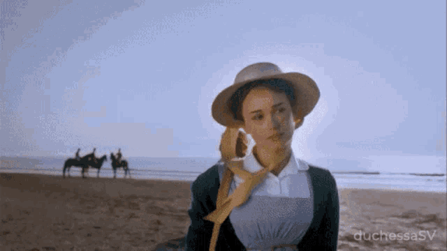 a woman in a hat stands on a beach with horses in the background ..