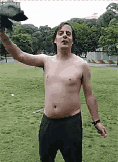 a shirtless man is standing in a grassy field holding up his arm