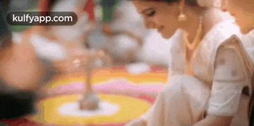 a woman in a white dress is sitting on the floor and making a circle with her hands .