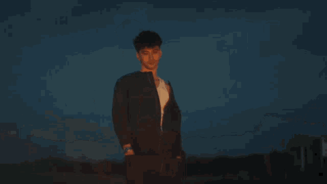 a man in a blue jacket stands in front of a fire at night