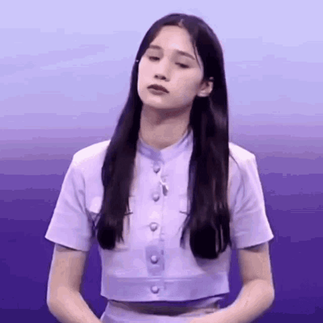 a woman with long black hair is wearing a purple crop top and a purple skirt .