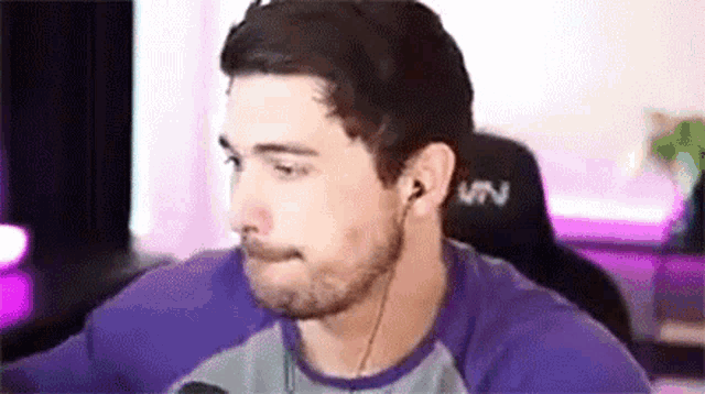 a man wearing headphones and a purple shirt is sitting in front of a computer screen .