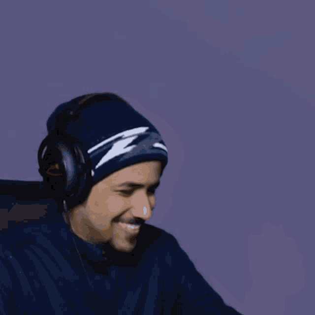 a man wearing headphones and a beanie holds a glass of beer