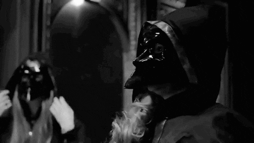 a black and white photo of a man wearing a mask and a hood smoking a cigarette .