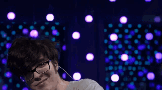 a young man wearing glasses and ear buds stands in front of a purple and blue background