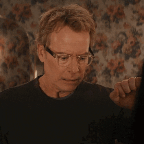 a man wearing glasses covering his mouth with his fist