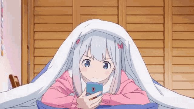 a girl is laying on a bed under a blanket while looking at her cell phone .