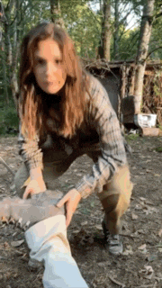a woman in a plaid shirt is kneeling down in the woods holding a pair of boots .