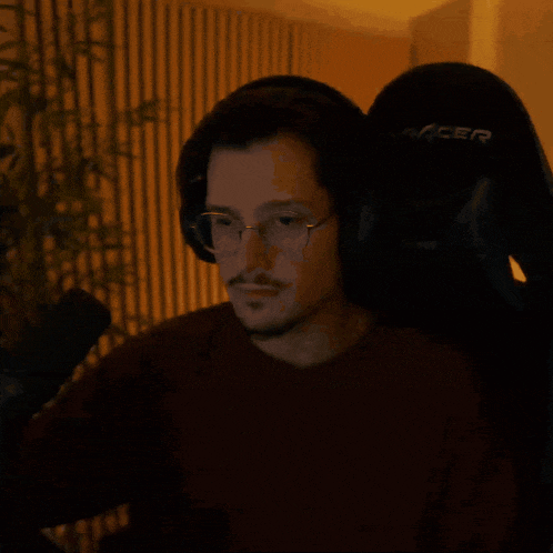 a man wearing headphones and glasses sits in a racer chair