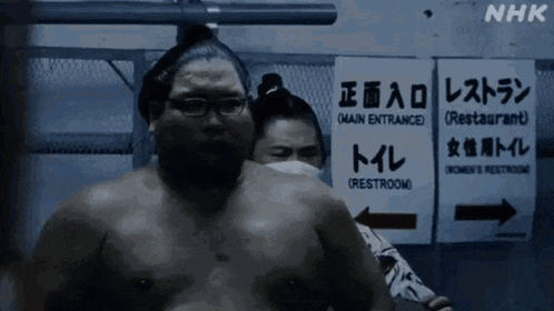 a sumo wrestler is standing in front of a sign that says " main entrance "