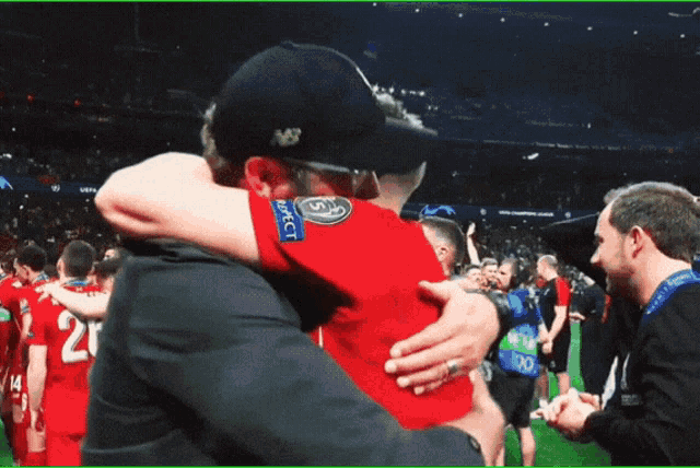 a man in a new balance hat hugging another man in a red shirt with the word respect on it