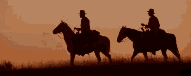 two cowboys are riding their horses in the sunset