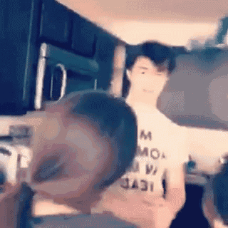 a man in a white t-shirt is standing in a kitchen with another man .