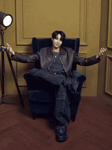 a man in a leather jacket is sitting in a chair with his legs crossed