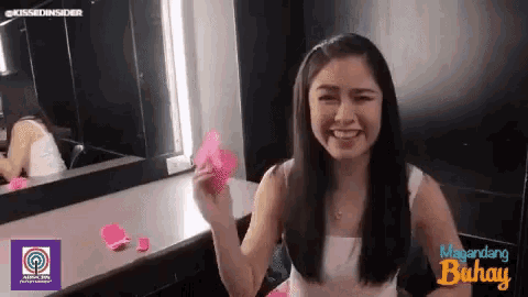 a woman is sitting in front of a mirror and smiling while holding a pink flower .