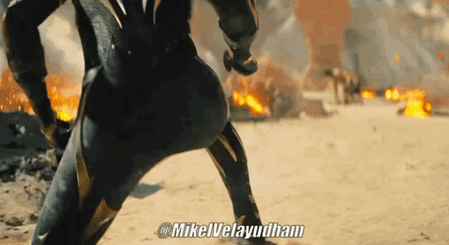 a man in a black and gold suit is standing in front of a fire and says mikeluleyudham