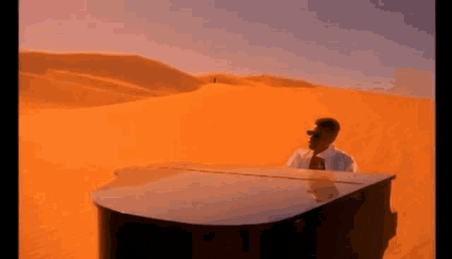 a man is playing a grand piano in the middle of a desert .