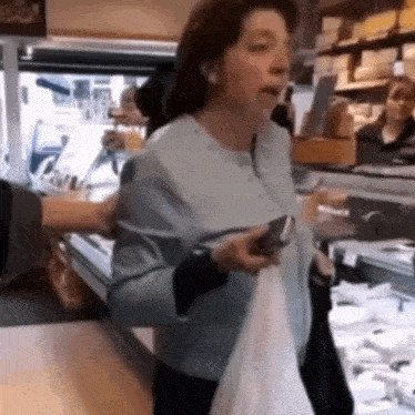 a woman in a blue jacket is holding a white bag and a cell phone .