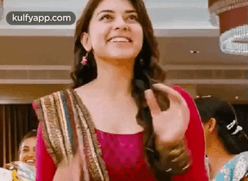 a woman in a pink dress is smiling and waving at the camera while standing in a room .