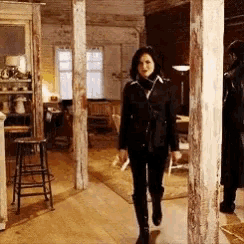 a woman in a black jacket and black boots is walking through a room .