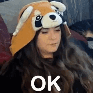 a woman wearing a red panda hat is sitting on a couch and making an ok sign .