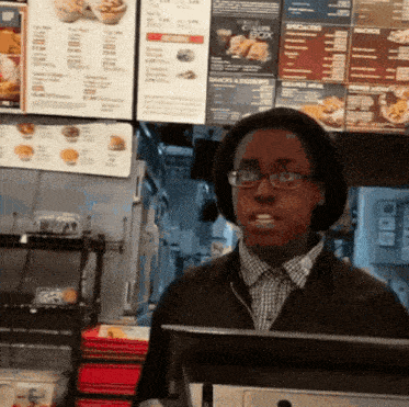 a man wearing glasses and a hat stands in front of a menu for a chicken box