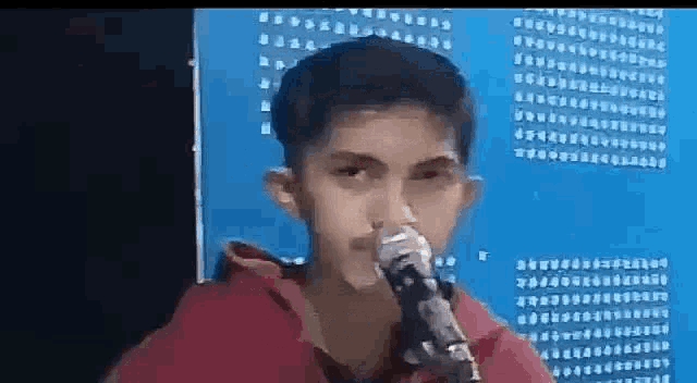 a young boy is singing into a microphone while wearing a red hoodie .