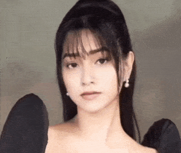 a woman in a black dress and earrings is looking at the camera .