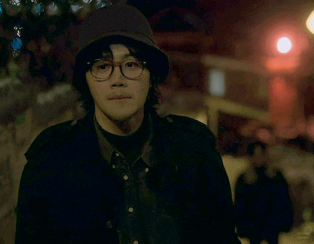 a man wearing glasses and a hat is standing in the dark .