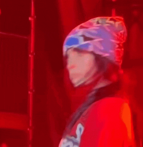 billie eilish is wearing a red shirt and a blue and white beanie while dancing on stage .