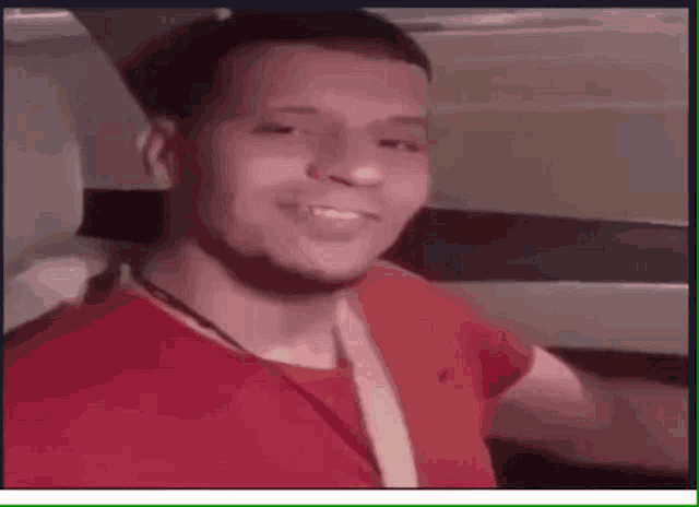 a man in a red shirt is sitting in the back seat of a car smiling .