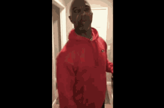 a man in a red hoodie is standing in a hallway and making a funny face .