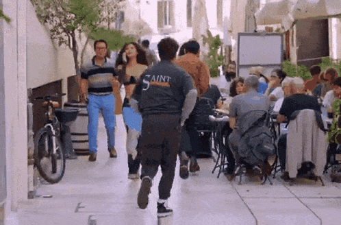 a man wearing a shirt that says saint is running down the street