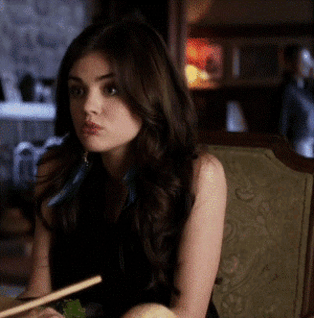 a woman in a black dress is sitting in a chair eating with chopsticks